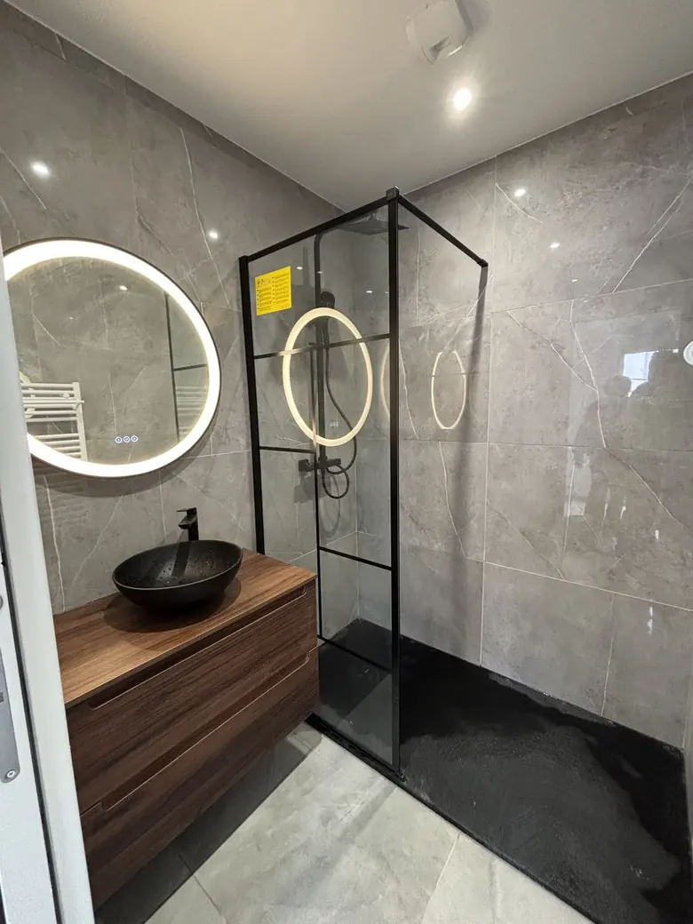 Salle d'eau avec douche vitrée et miroir rond lumineux