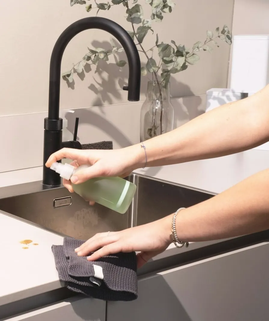 Mains qui nettoient le plan de travail d'une cuisine moderne avec une lavette et un vaporisateur
